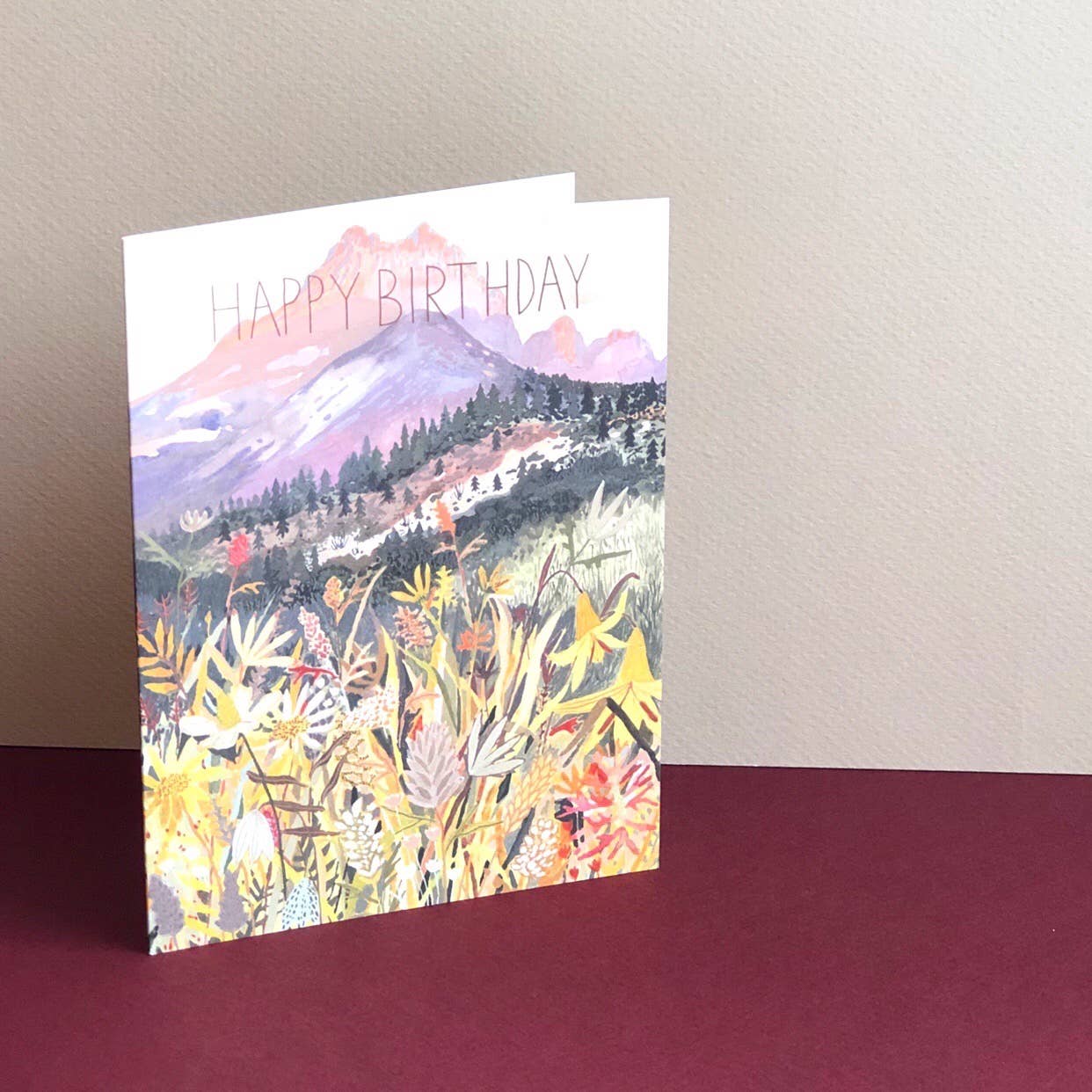 Greeting card says Happy Birthday with mountain and floral design background